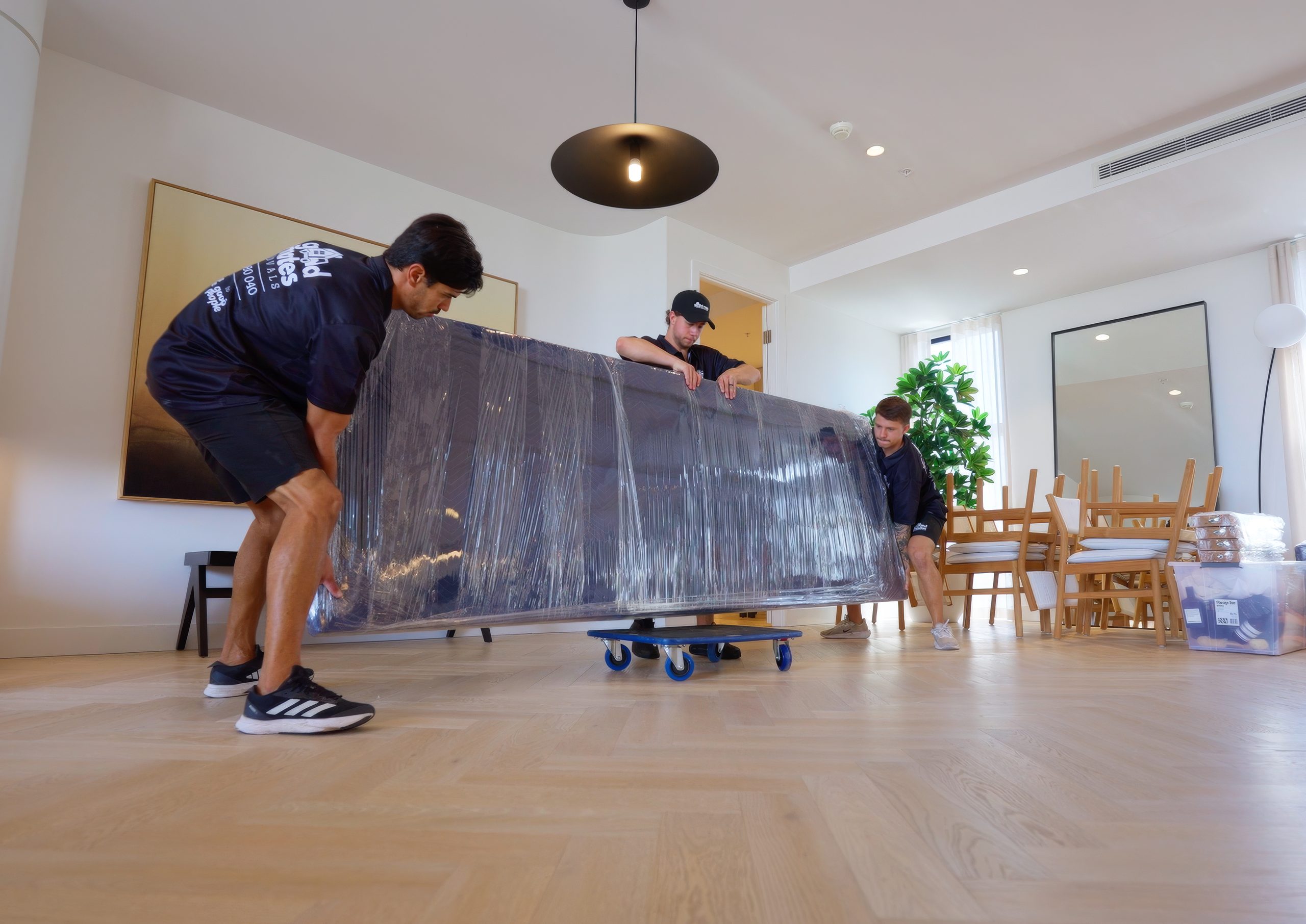 Good Mates removalists carrying a piece of furniture wrapped in protective padding and plastic on a dolly